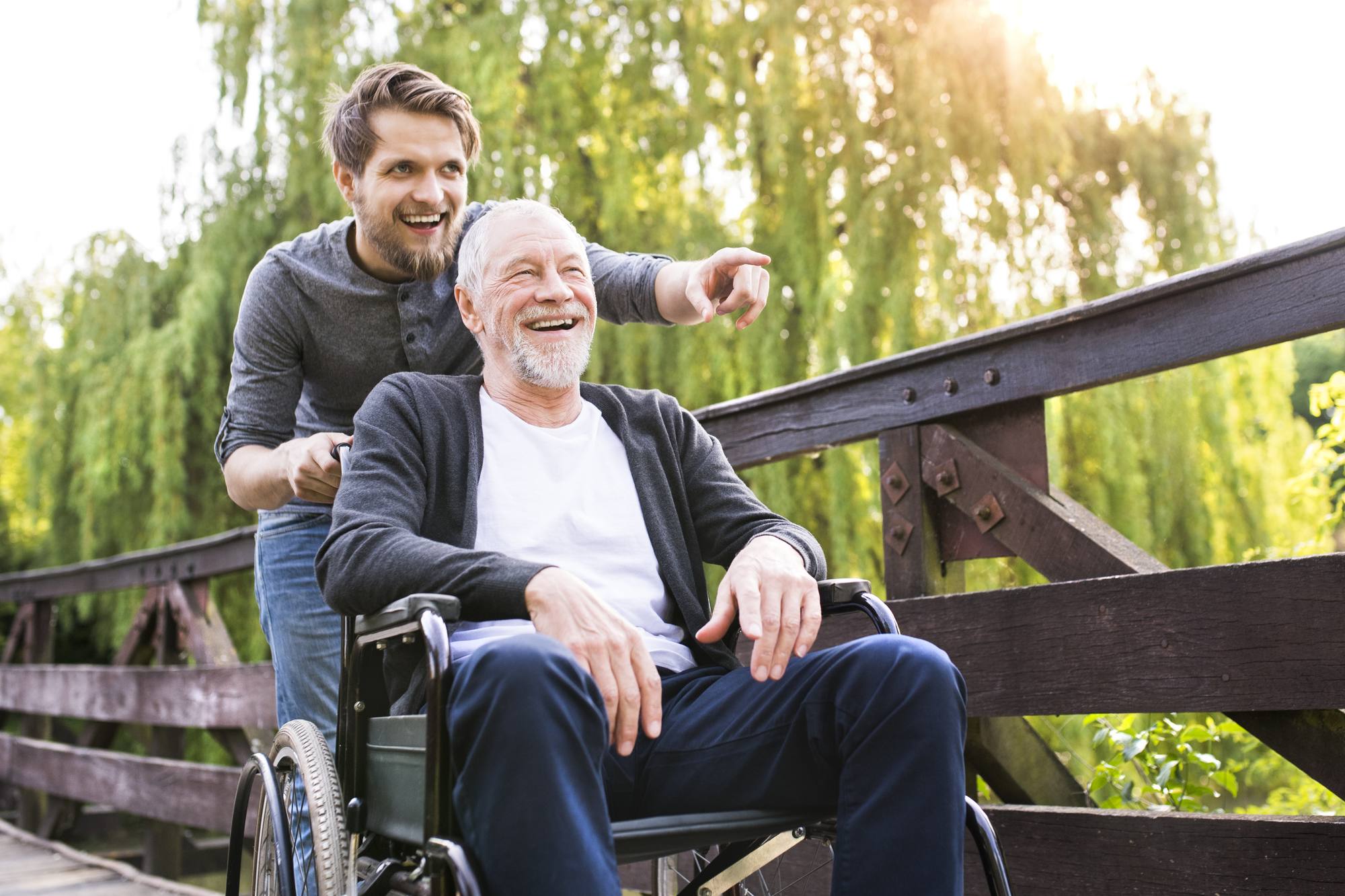young person walking with father pushing him in wheelchair at park
